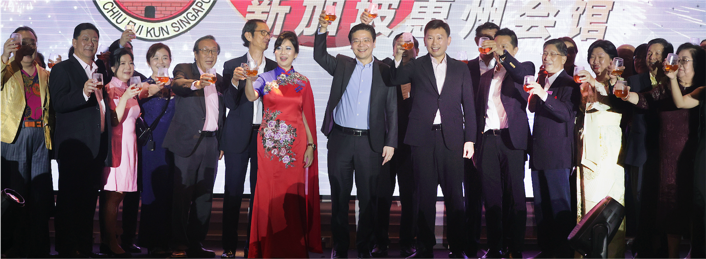 Group of people in formal attire toasting with drinks in front of a backdrop.